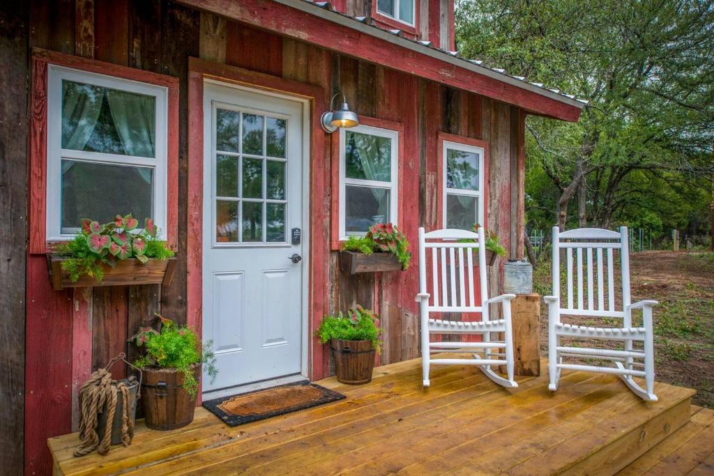 韦科Cozy Cabin Little Red Hen 12 min to Magnolia的红色的房子,有两把白色椅子和门