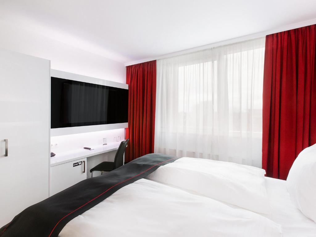 汉诺威DORMERO Hotel Hannover-Langenhagen Airport的一间卧室配有一张带红色窗帘的床和电视。
