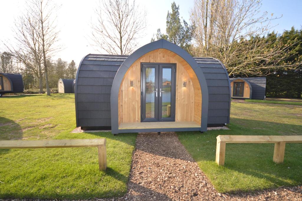 伯青顿Camping Pods, Birchington Vale Holiday Park的田野上的小房子,有两把长椅