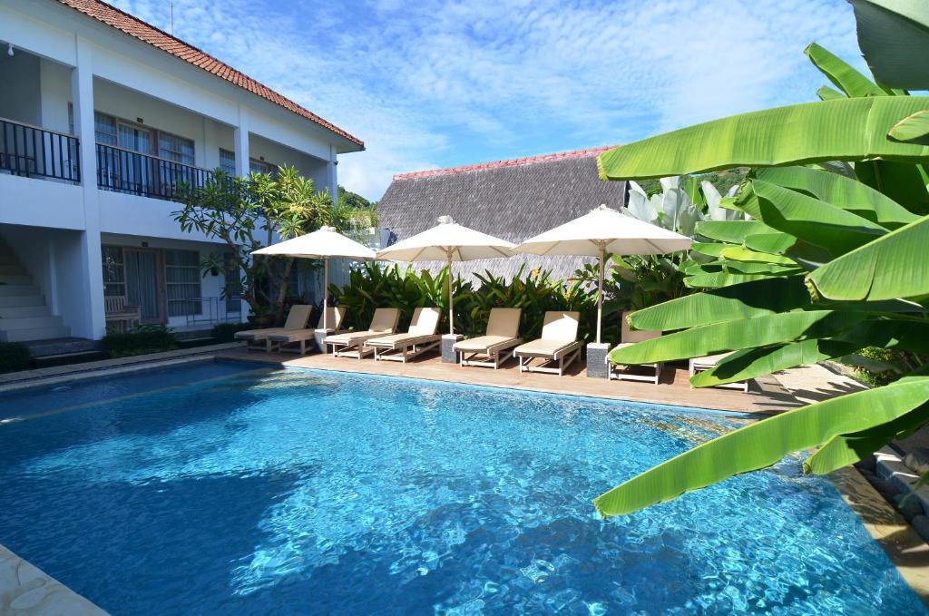 龙目岛库塔Lavella Villas Kuta Lombok的一座带椅子和遮阳伞的游泳池位于一座建筑旁边