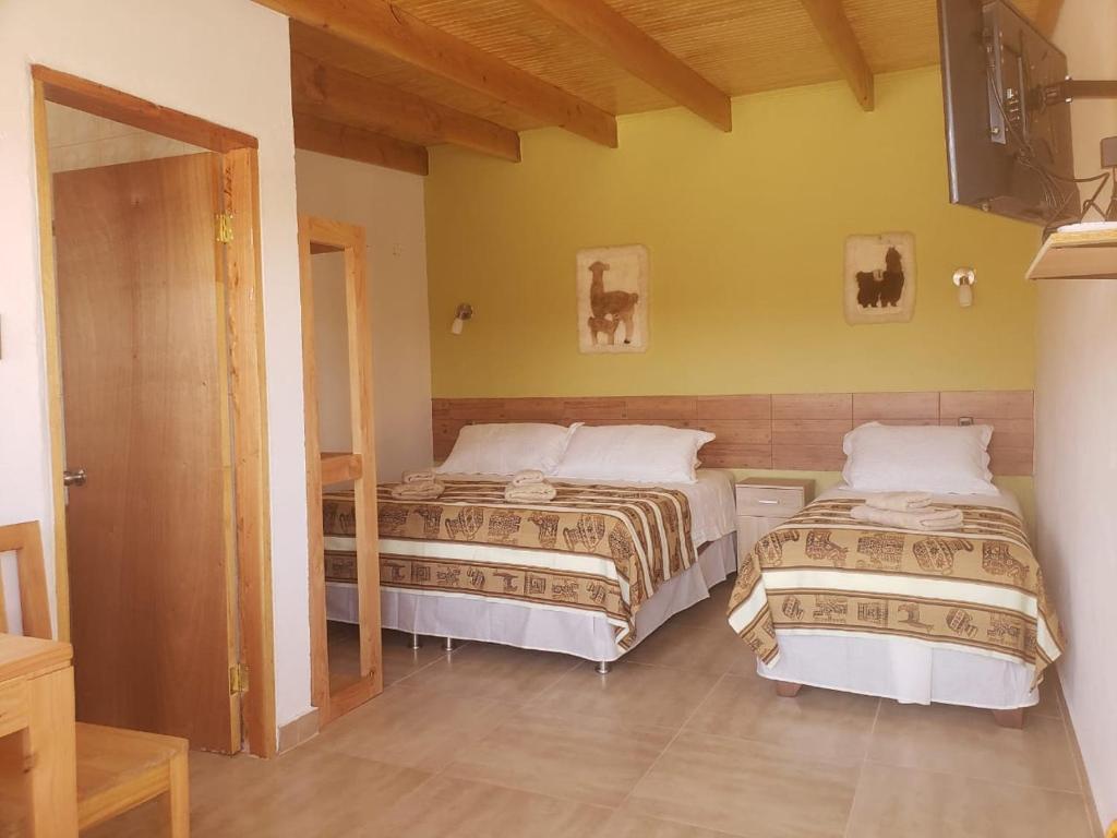 圣佩德罗·德·阿塔卡马Hostal Pablito 2的一间卧室设有两张床,墙上配有电视。