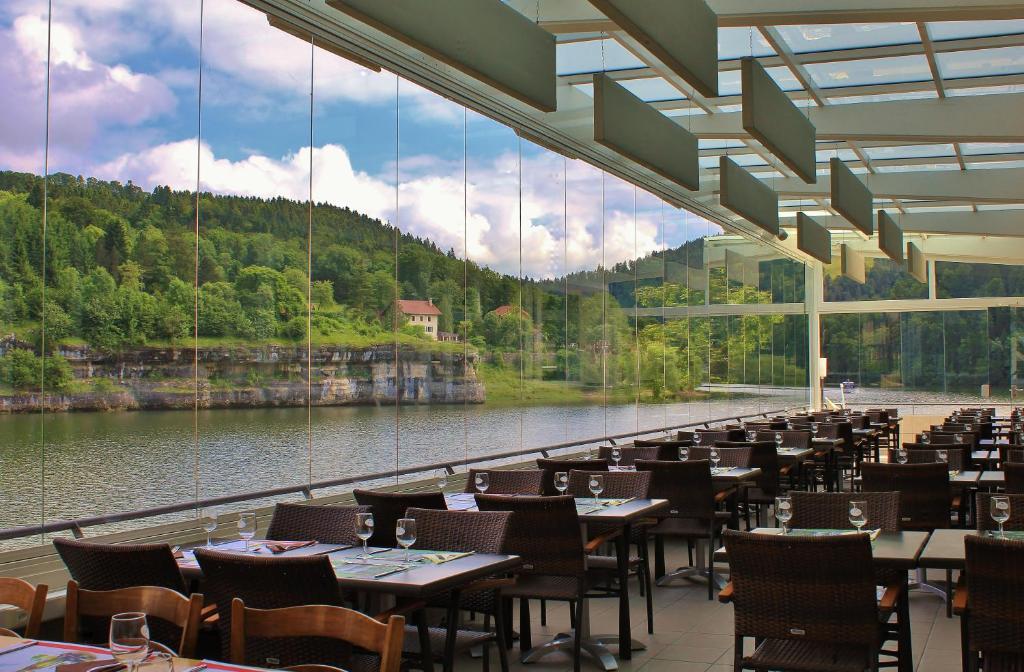 莱斯布里内特Hotel Les Rives Du Doubs的餐厅设有桌椅和大窗户。