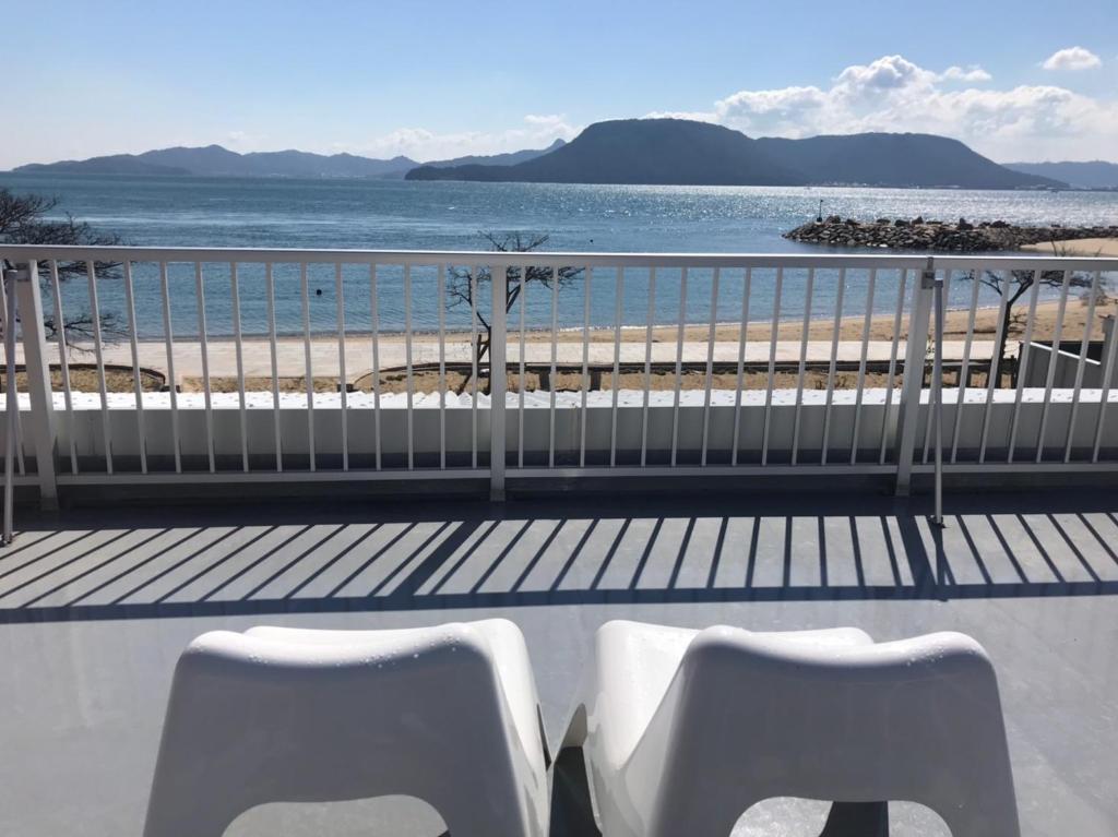 高松Megijima Island Guesthouse & cafe Megino的两把白色椅子坐在俯瞰着海滩的阳台上