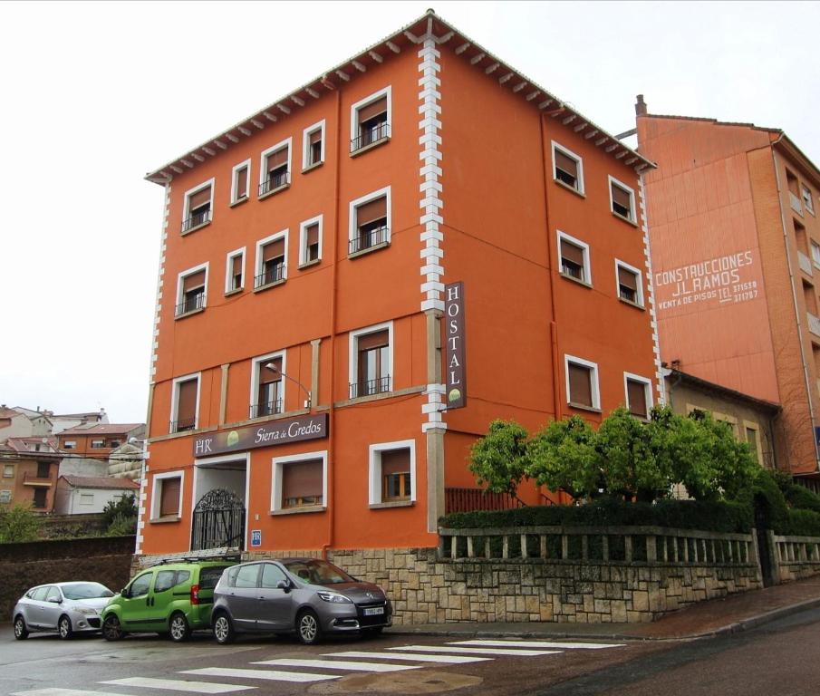 阿雷纳斯德圣佩德罗Hostal Sierra de Gredos的一座橙色的建筑,前面有汽车停放