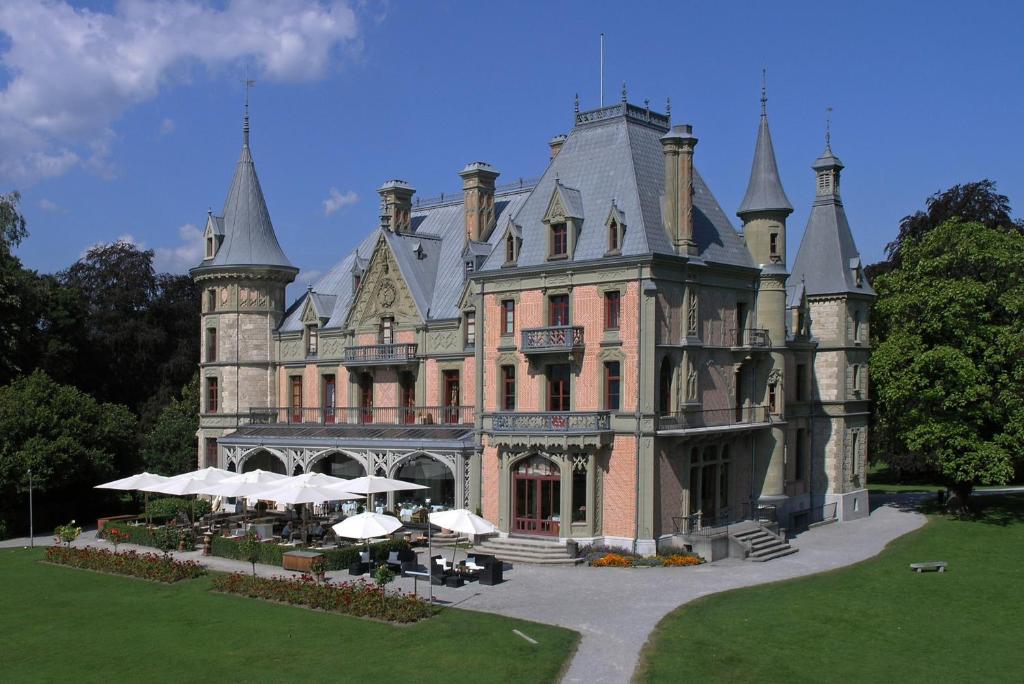 图恩Schloss Schadau - Swiss Historic Hotel的前面设有桌子和遮阳伞的城堡
