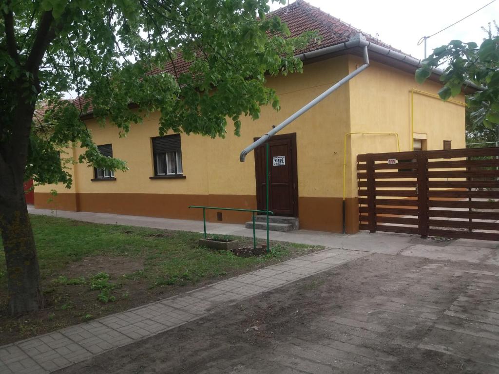 MezőkovácsházaHársfák的黄色的房子,前面有栅栏和长凳