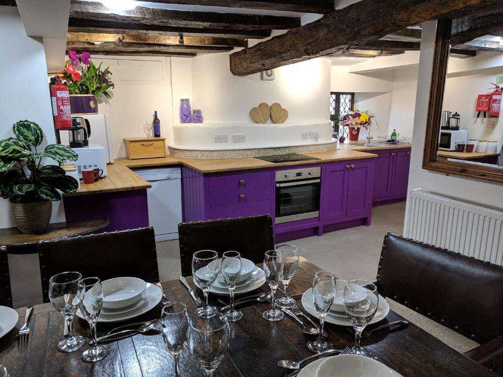 斯特劳德Cotswolds Valleys Accommodation - Medieval Hall - Exclusive use character three bedroom holiday apartment的厨房配有紫色橱柜和带酒杯的桌子