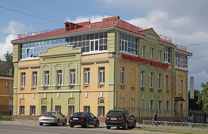 伊万诺沃Zubkovskiy Hotel的一座黄色的建筑,前面有汽车停放