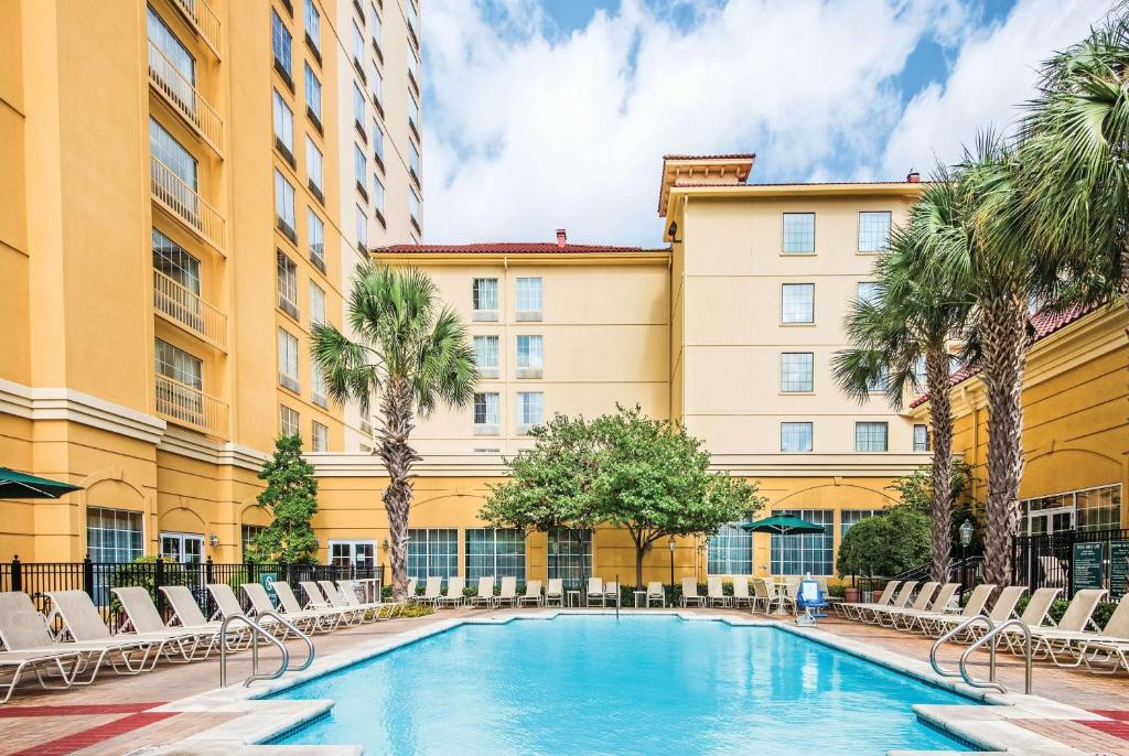 圣安东尼奥La Quinta Inn & Suites by Wyndham San Antonio Riverwalk的一座游泳池位于一座带椅子和棕榈树的建筑前