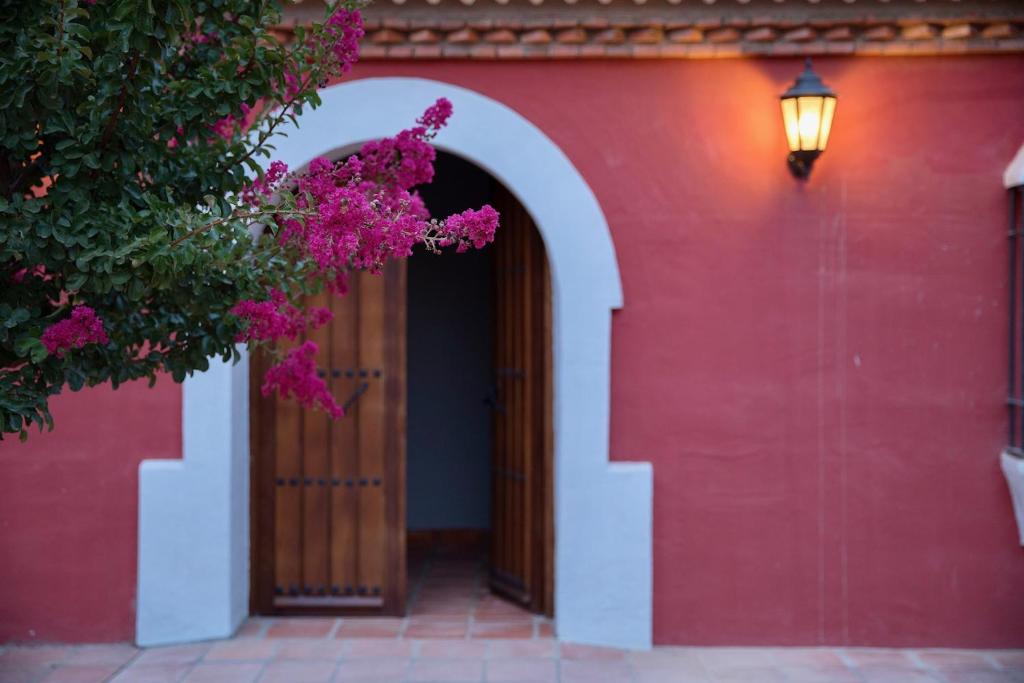 ValdecaballerosHotel Rural Las Tejuelas的红色的建筑,有扇粉红色花朵的门