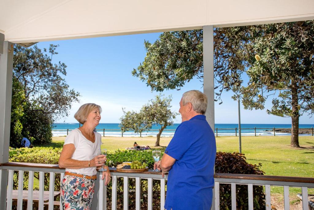 伍尔古尔加Woolgoolga Beach Holiday Park的有一对年纪较大的夫妇站在一个门廊上,眺望着海滩