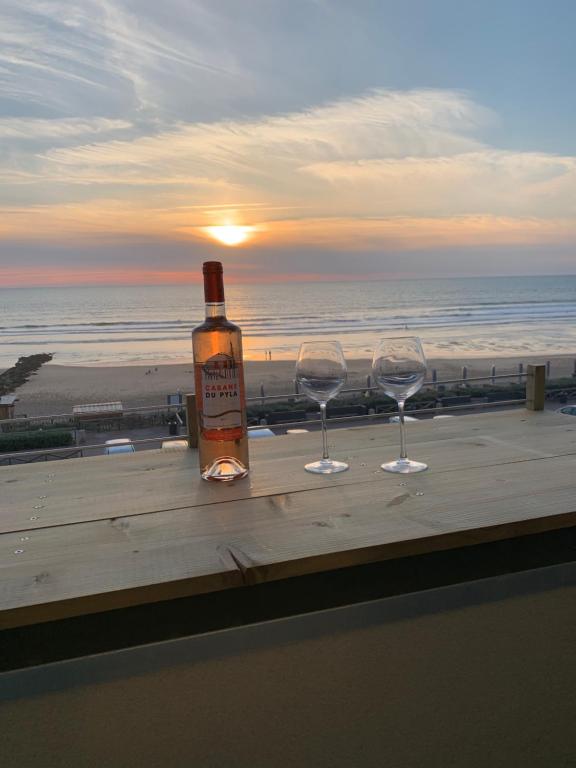 拉卡诺LACANAU FRONT DE MER的一瓶葡萄酒和两张玻璃杯,放在桌子上,上面有沙滩