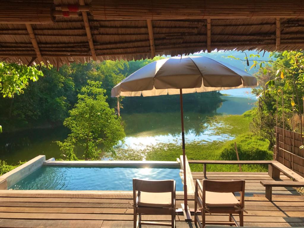 宋卡塔省帕拉度假村的一个带两把椅子和一把遮阳伞的庭院,毗邻一个游泳池