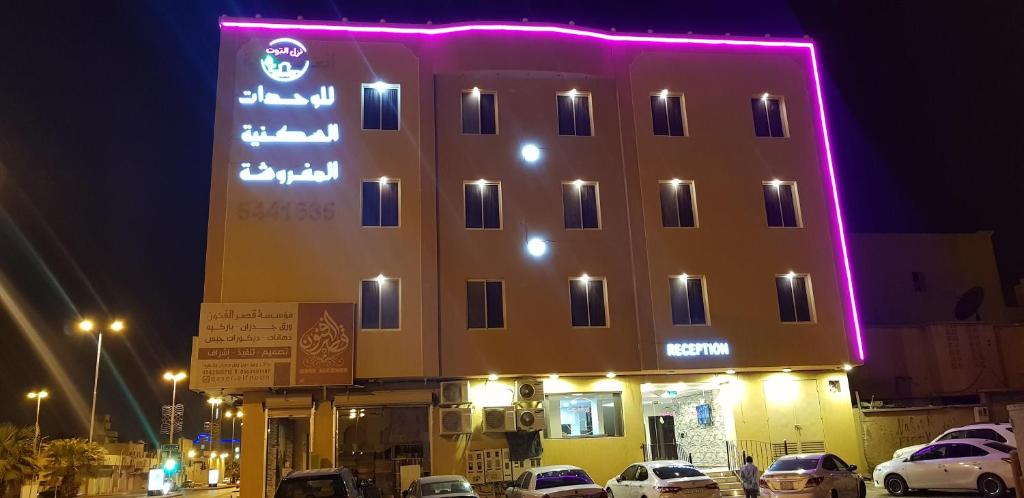 阿尔卡吉Nozul Al Tout Furnished Apartments的一座有照明的建筑,前面有汽车停放