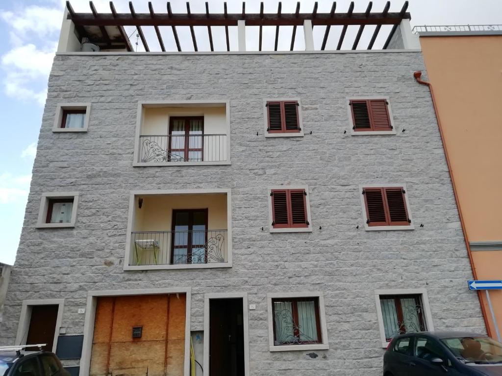 奥尔比亚B&B Nino的灰色的建筑,有红色百叶窗和窗户