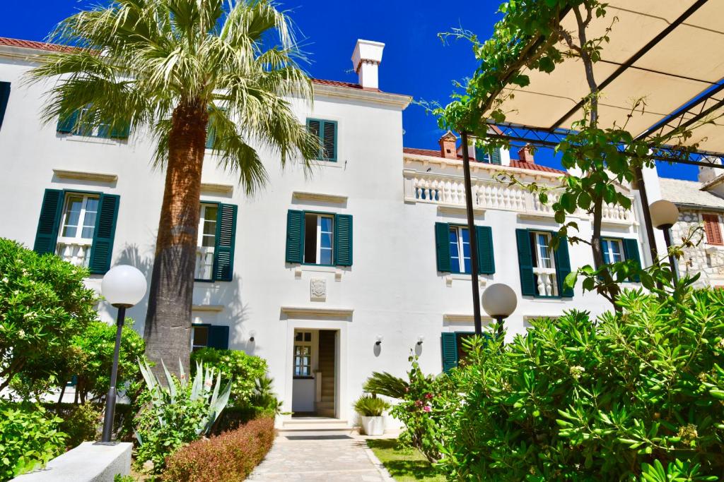 波尔Villa Giardino Heritage Boutique Hotel Bol的白色的房子,有绿色百叶窗和棕榈树
