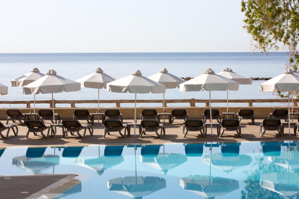 利马索尔和谐湾酒店的海滩上的游泳池配有遮阳伞和椅子