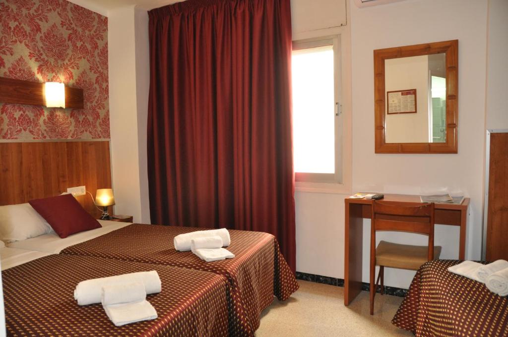 罗列特海岸Hostal - Pensión El Amigo的酒店客房设有两张床、一张桌子和一面镜子