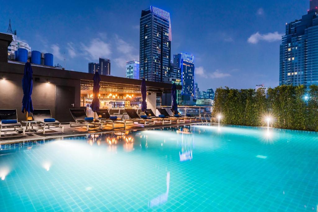 曼谷The Key Premier Hotel Sukhumvit Bangkok的一个带椅子的大型游泳池,享有城市天际线
