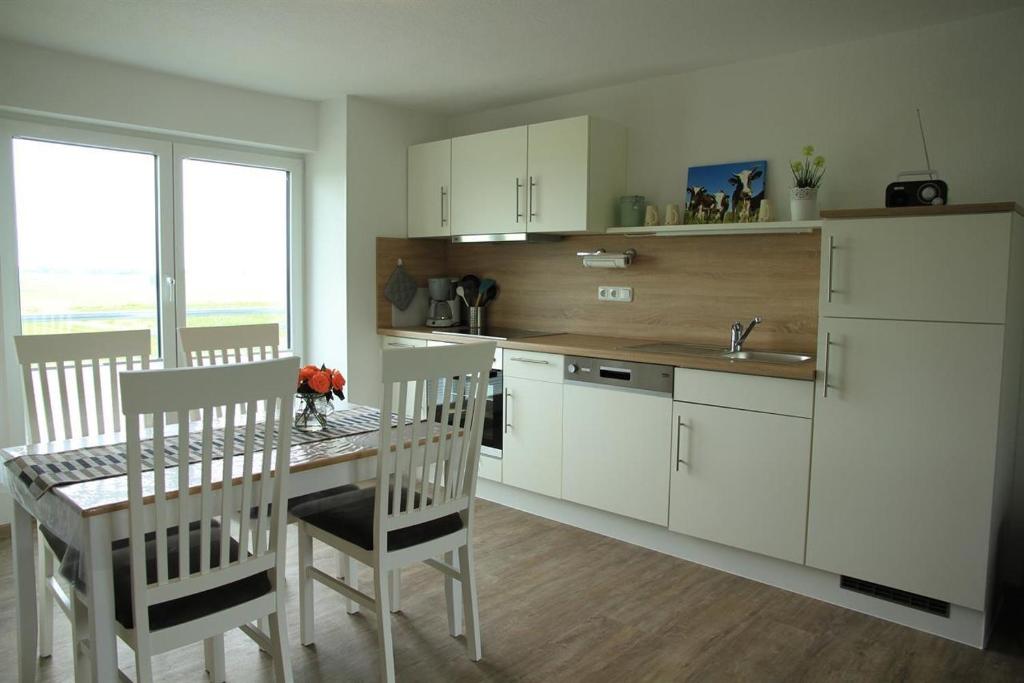 VollerwiekHaus am Meer的厨房配有白色橱柜和桌椅
