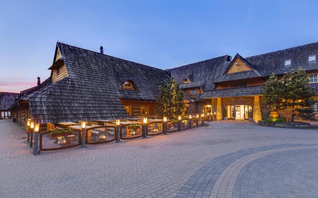 塔干尼采Kocierz Resort - Hotel的一座大型木质建筑,前面有灯