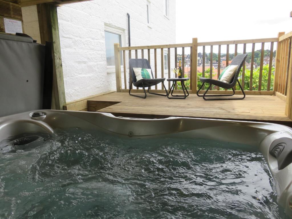 惠特比Esk Cottage - Cyanacottages的甲板上的热水浴池配有两把椅子和一张桌子