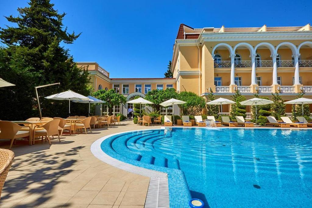 敖德萨德尔马宫酒店的一座带椅子和遮阳伞的游泳池位于一座建筑旁边