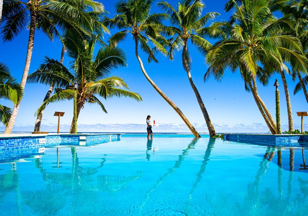 拉罗汤加小玻利尼西亚度假酒店的站在棕榈树泳池前的人