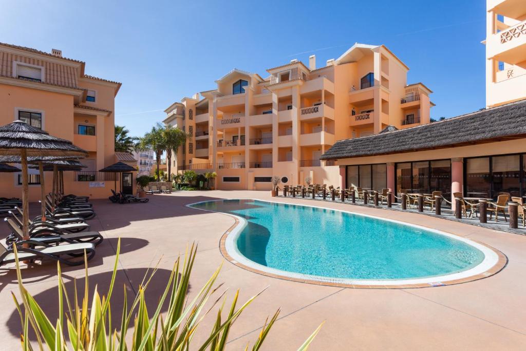 卢斯Aum Praia da Luz Resort Apartment的一座带椅子的度假村游泳池以及一座建筑