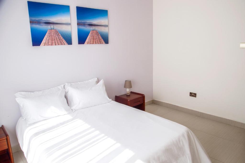 卢萨卡MC Apartments的卧室配有一张白色床,墙上挂有两张照片