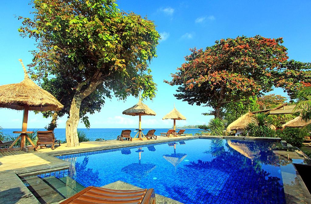 圣吉吉龙目岛日落酒店的毗邻大海的带椅子和遮阳伞的游泳池