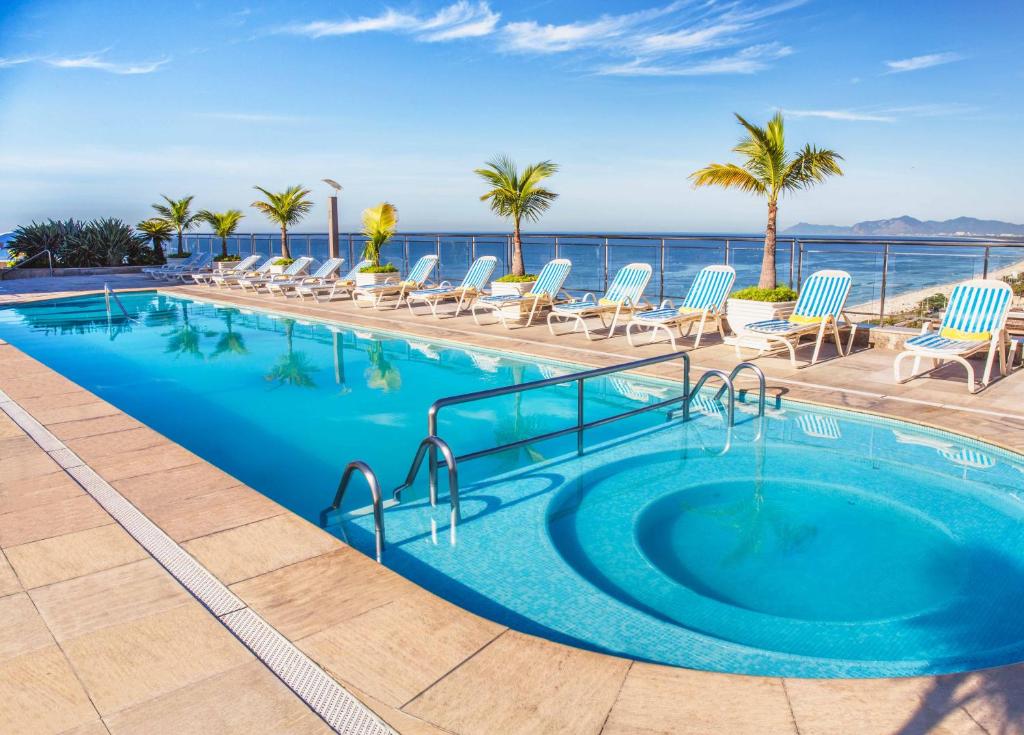 里约热内卢温莎芭拉酒店的一个带椅子的游泳池,背景是大海