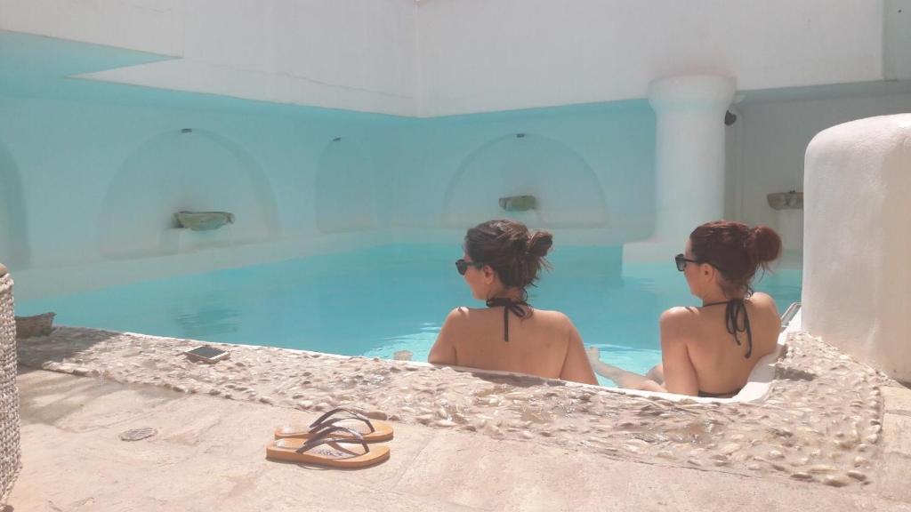 提诺斯阿尔塔纳精品酒店的两个女人坐在一个游泳池里,穿着凉鞋