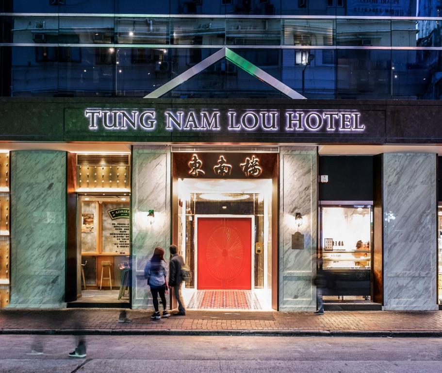 香港Tung Nam Lou Art Hotel的两个人站在商店外面,拿着一扇红色的门