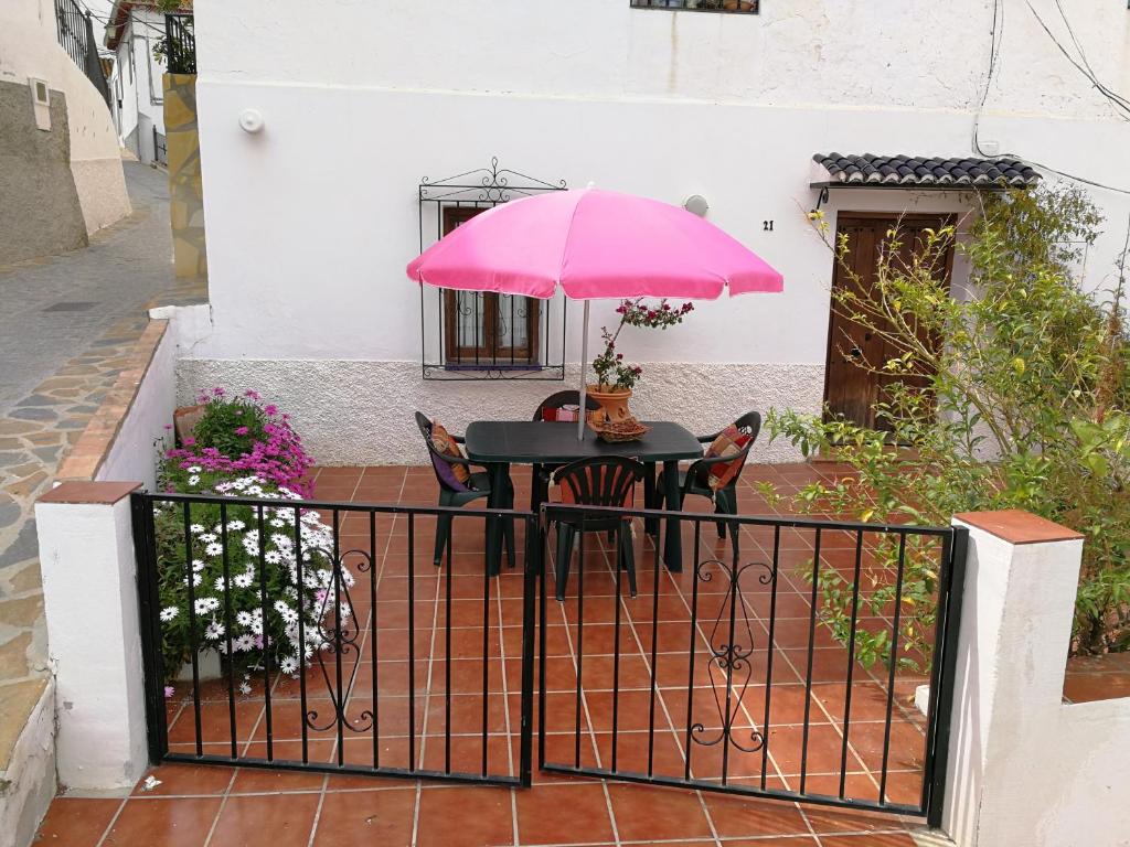 AlmácharCasa en pueblo de montes de Málaga a 15km de playa的围栏上的一张桌子和一把粉红色的伞