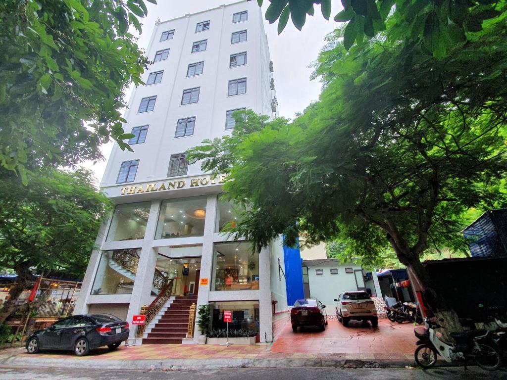 吉婆岛Cat Ba Thailand Hotel的一座高大的白色建筑,前面有汽车停放