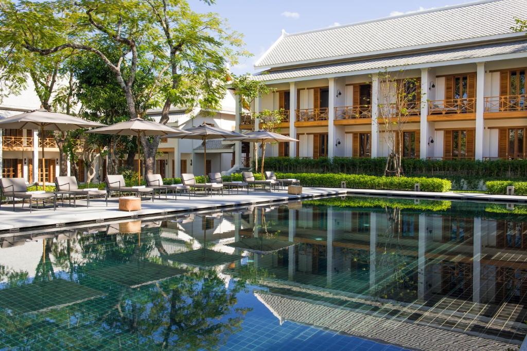 琅勃拉邦Avani+ Luang Prabang Hotel的一座带椅子和遮阳伞的大楼前的游泳池
