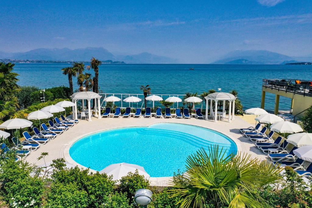 代森扎诺-德尔加达利都国际酒店的一个带椅子和遮阳伞的游泳池以及大海