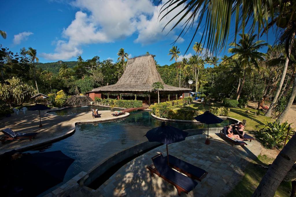 贝卡岛Beqa Lagoon Resort的度假村的游泳池,有人坐在遮阳伞下
