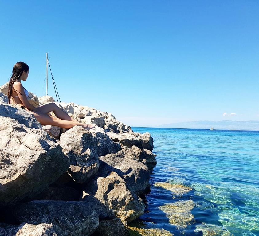 锡尔巴岛Kuća za odmor Silba的坐在水边的岩石上的女人