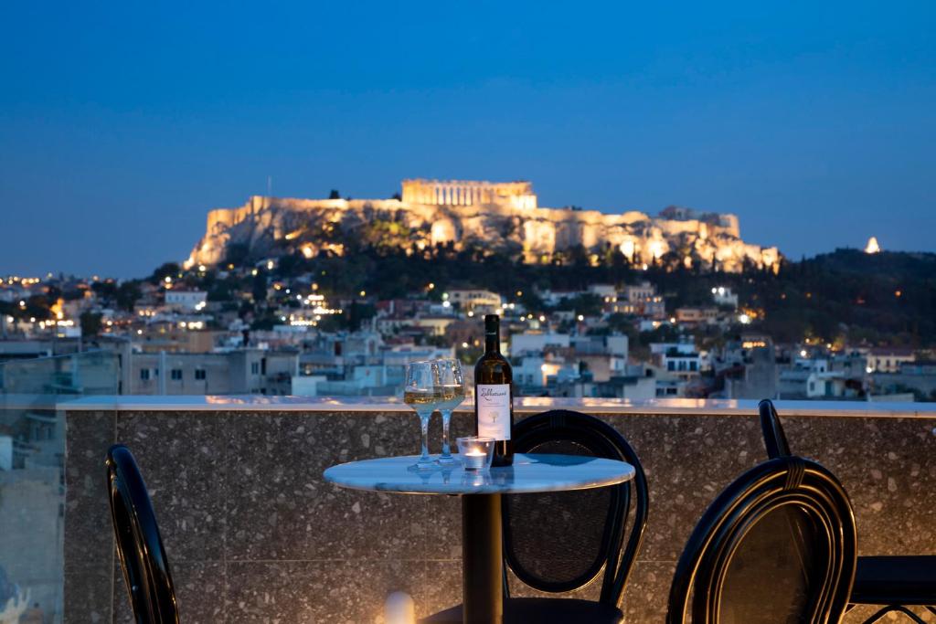 雅典The Pinnacle Athens的一张桌子上摆放着一瓶葡萄酒,还有两把椅子