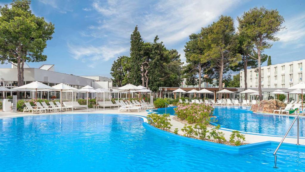 希贝尼克Amadria Park Family Hotel Jakov的一座带白色椅子和遮阳伞的酒店游泳池