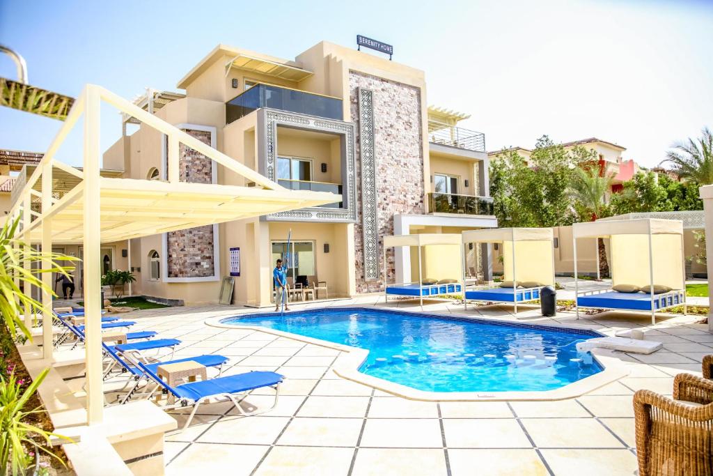 赫尔格达Serenity Home Hurghada的一座带蓝色躺椅的建筑前的游泳池