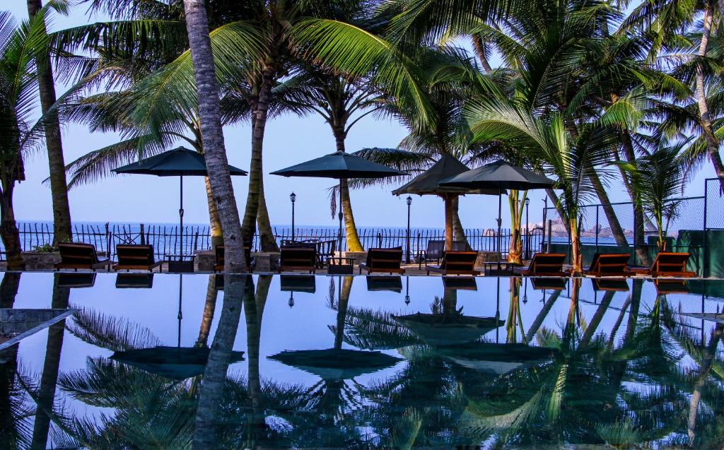 希克杜沃Hikka Sandy Pearl Beach Resort的一个带椅子和遮阳伞的游泳池以及棕榈树