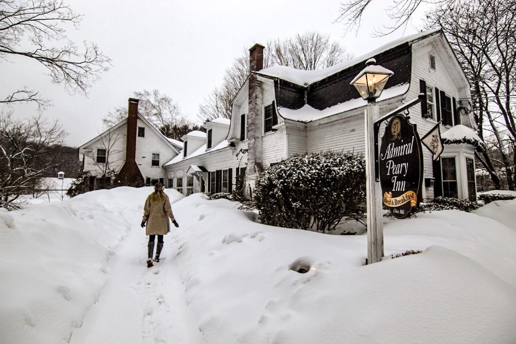 FryeburgAdmiral Peary Inn的一位女人在房子前面的一条雪覆盖的街道上行走