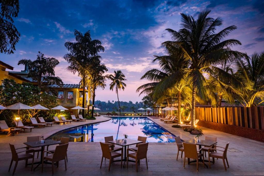 科尔瓦海滩旁贝莱扎酒店的一个带桌椅的度假村游泳池,并种植了棕榈树