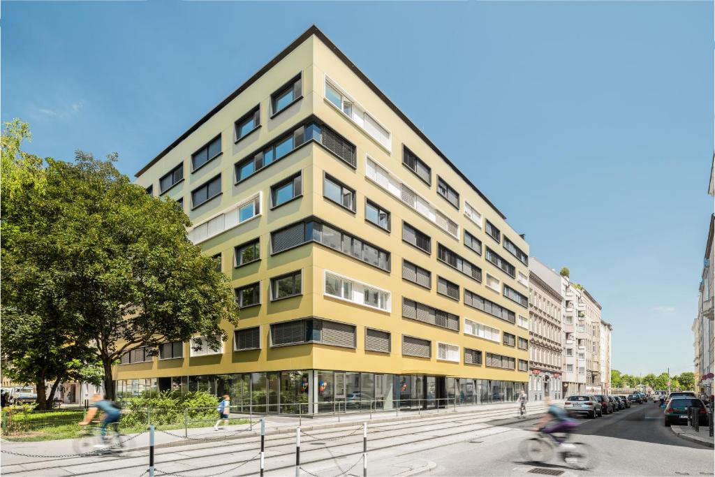 维也纳myNext - Hotel Leo的一条城市街道上的黄色建筑,人们骑着自行车