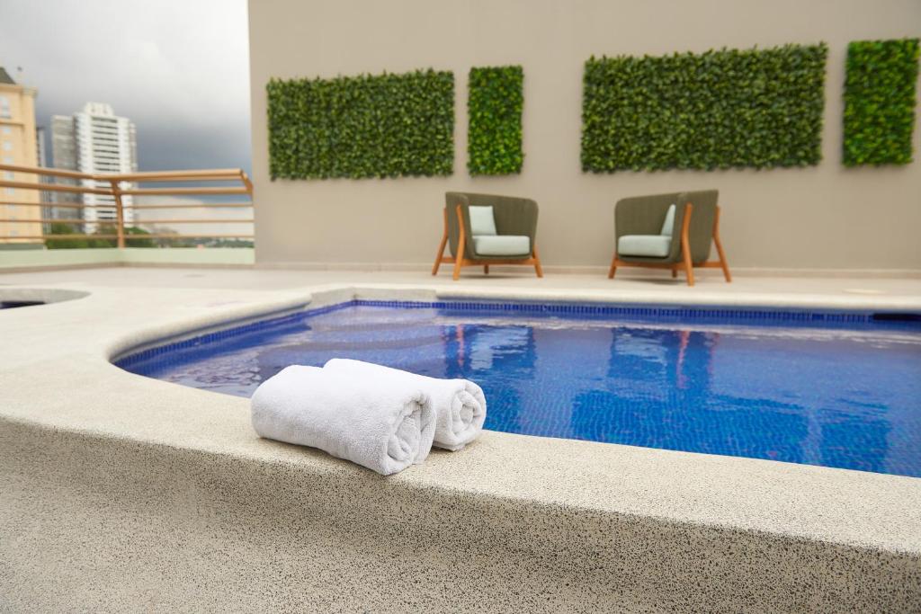 圣萨尔瓦多Suites las Palmas, Hotel & Apartments.的大楼内一个带两把毛巾和椅子的游泳池
