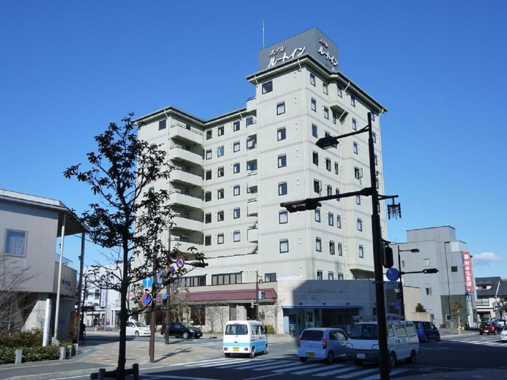 岛田岛田站前路线酒店的一座高大的白色建筑,前面有汽车停放
