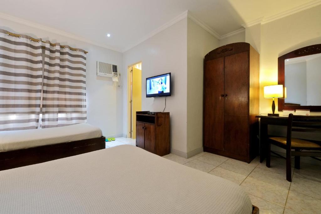 宿务攀升宫酒店的一间卧室配有一张床、一张书桌和一台电视
